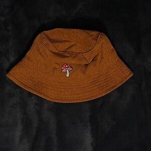 Corduroy brown bucket hat with a little red mushroom in the front.